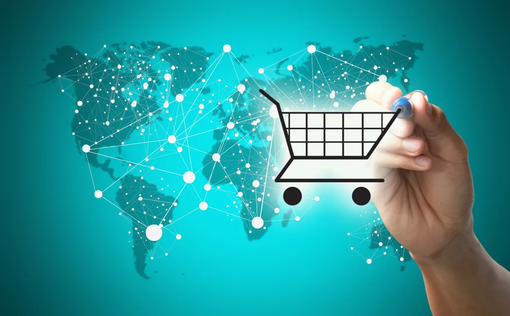 A hand drawing a shopping cart icon in front of a digital map representing the global reach of eCommerce networks.