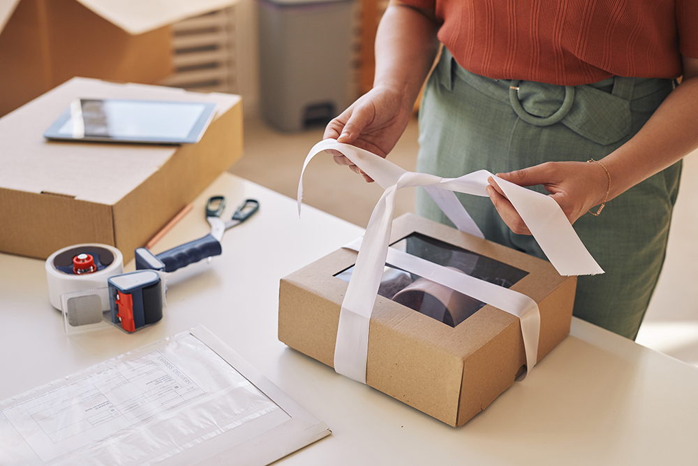 A woman carefully opens a beautifully wrapped box, showcasing elegant product packaging with a ribbon.